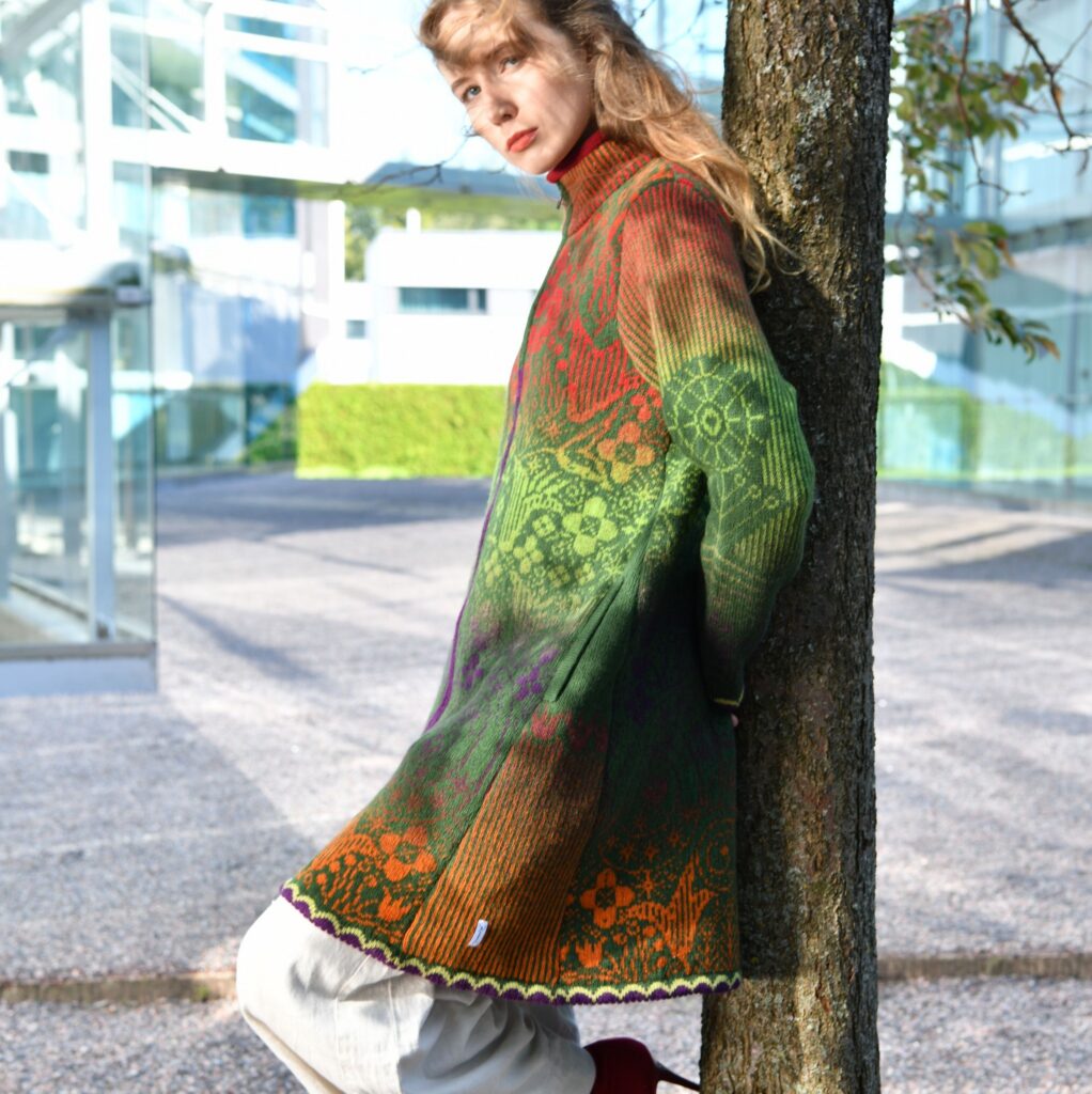 kauni design model leaning on a tree wearing a green and brown gradient wool cardigan