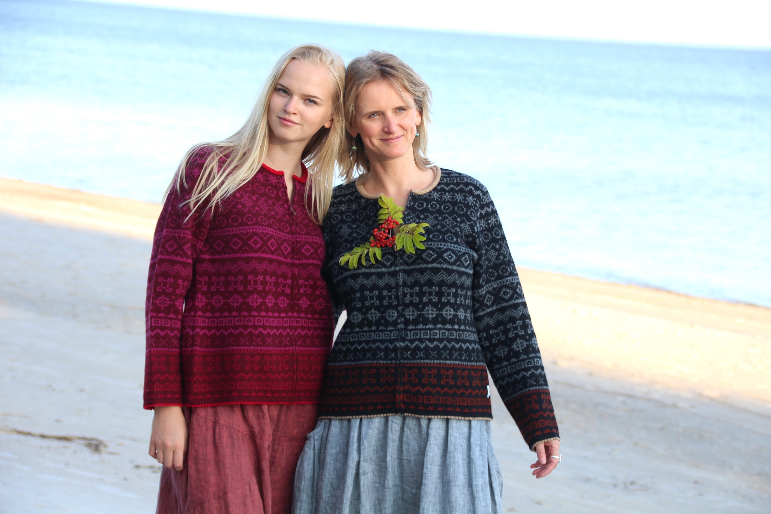 blonde daughter and mother on Baltic beach wearing short red and black woollen cardigans
