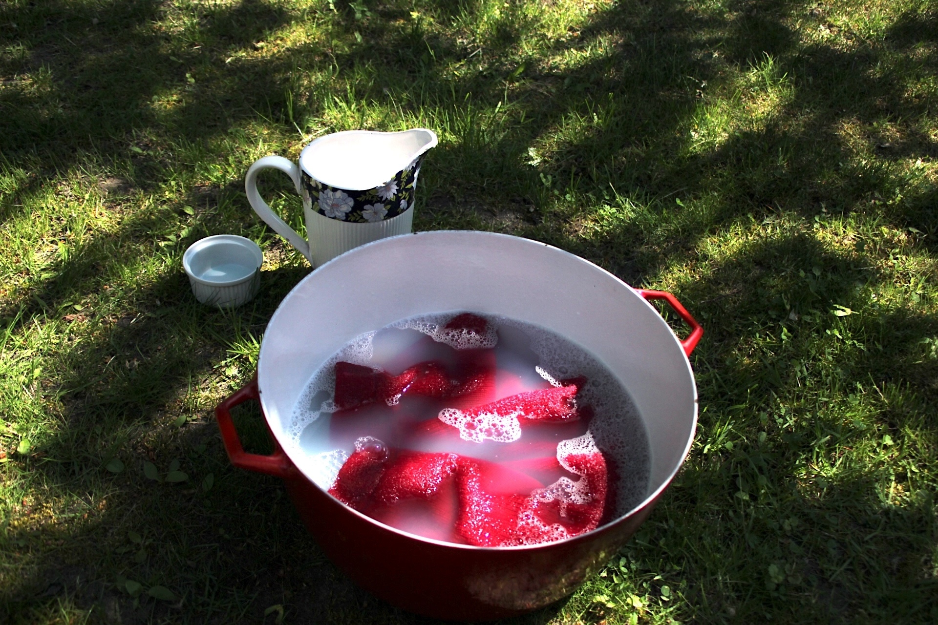 a red bowl with water and wool detergent, and a red wool garment on the grass