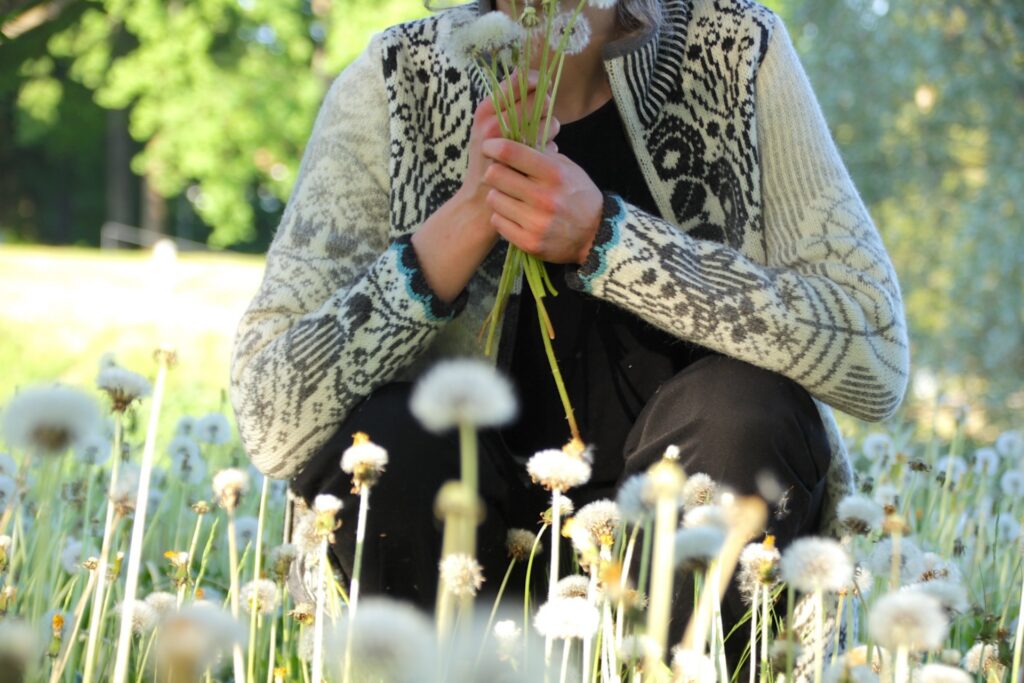 a model in a white woollen sweater with flowers holding a bouquet of dandelion puffballs on a sunny spring day
