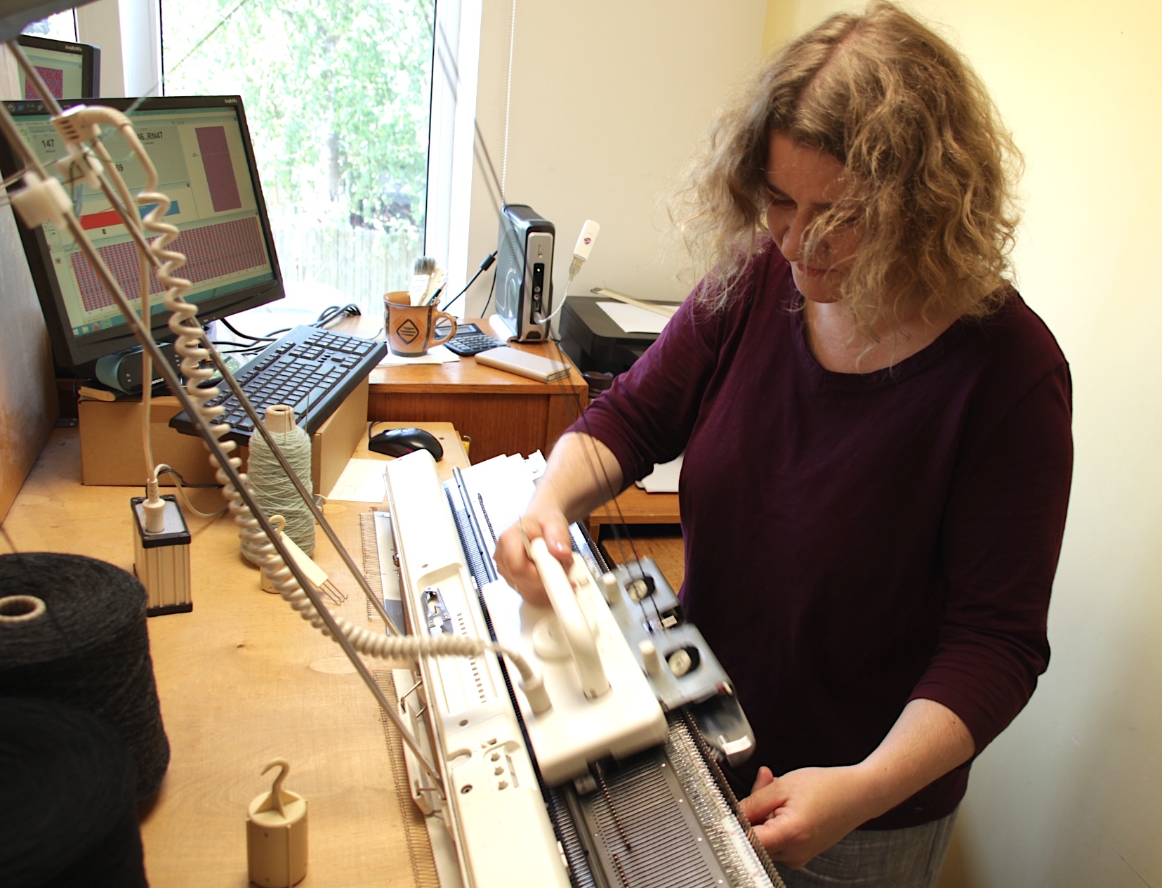 a knitter knitting a wool garment on a knitting machine