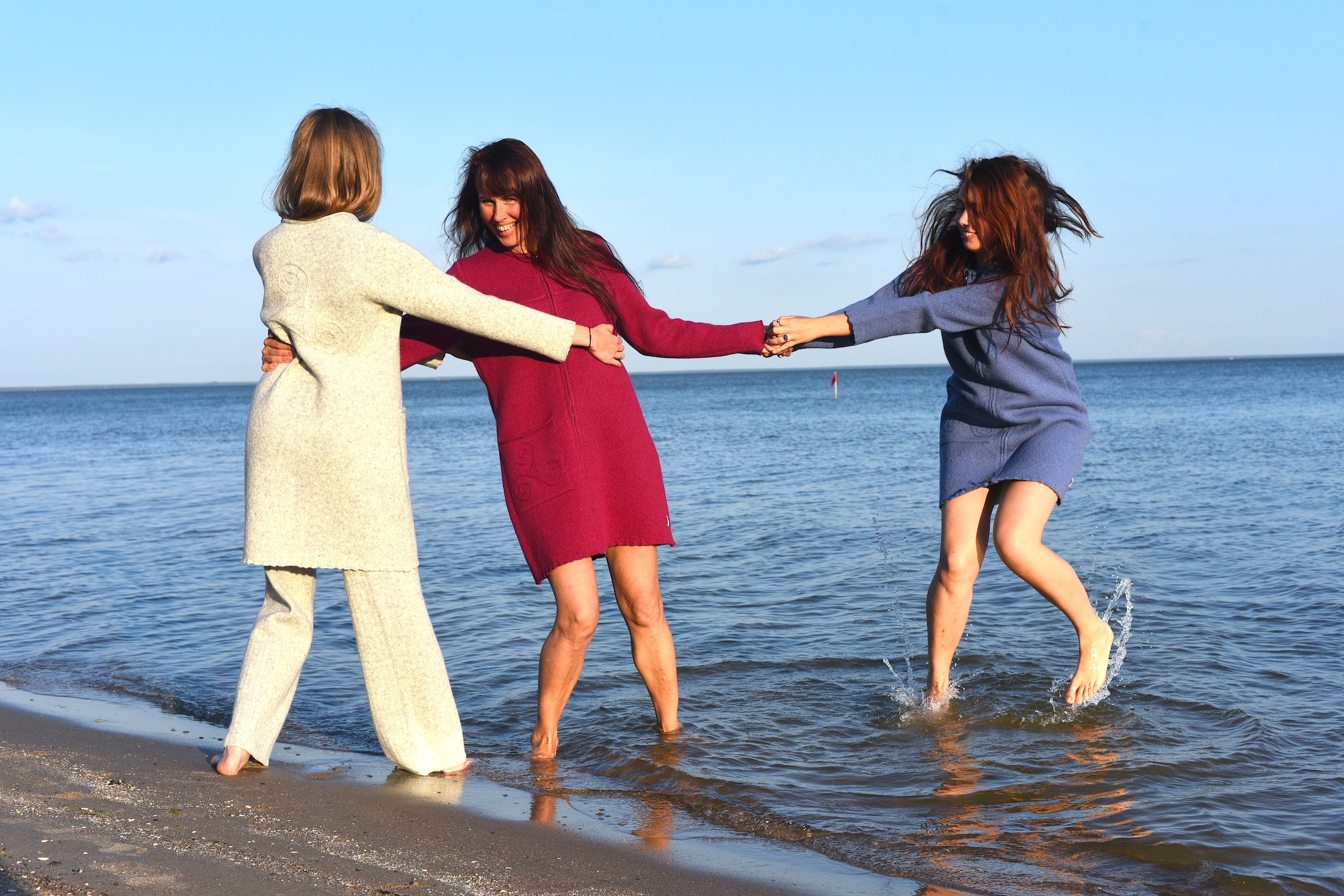 3 women in wool design standing with their feet in the sea