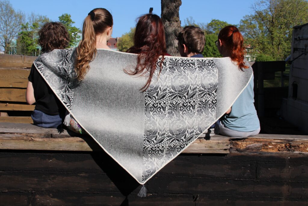 kauni 5 kids sitting on a boat with their backs wrapped in kauni wool shawl