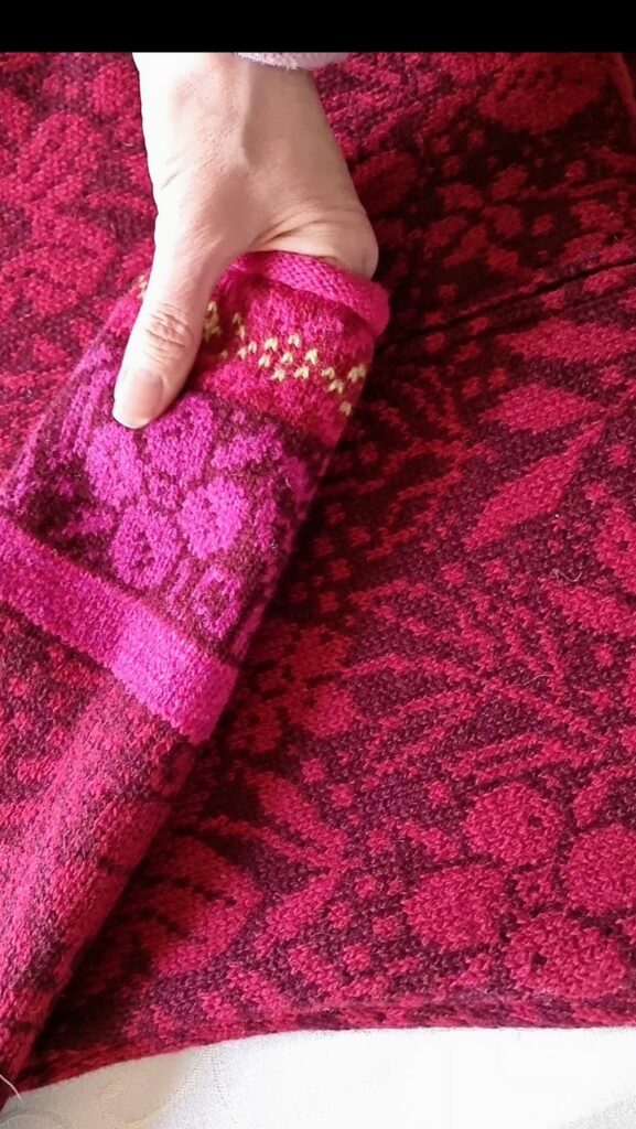 close up detail of hands and red wool cardigan with flowers